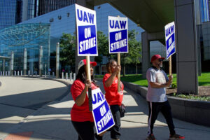 Black man and two women hold blue and white signs saying UAW ON Strike